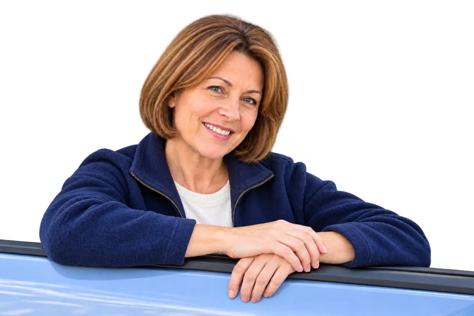 A smiling driving instructor leaning towards the open passenger window of a parked car